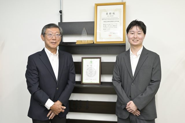 表彰状の前でほほえむ新電力新潟株式会社の吉澤洋さんと根岸優太さん