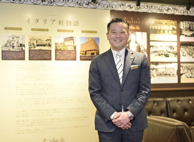 ホテルイタリア軒創業150周年を記念した歴史展示物の前でほほえむ山田伸吾氏