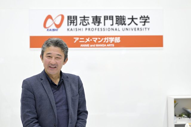 ロゴの前でほほえむ開志専門職大学アニメ・マンガ学部 学部長の成田 兵衛氏