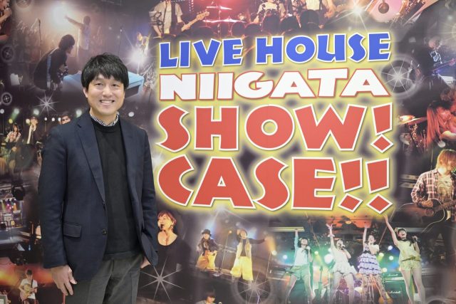 パネルの前でほほ笑む国際音楽・ダンス・エンタテイメント専門学校副校長の山本 雄太氏